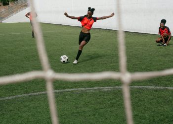 girl in red shirt and black shorts kicking a soccer ball